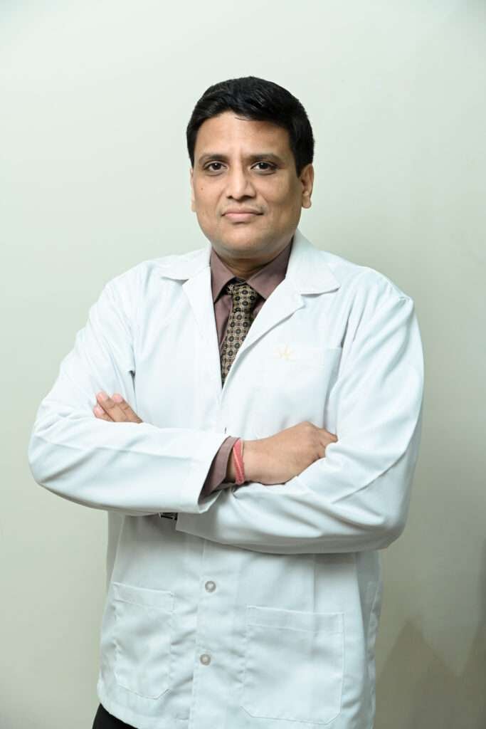 A doctor in a white lab coat with arms crossed, standing against a light background.